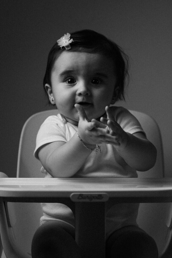 Black and white photo of a cute baby clapping in a high chair with a joyful expression.