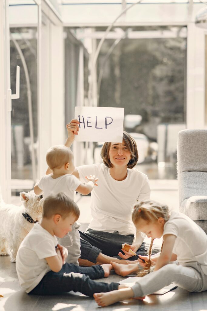 Woman holding placard with sign help while looking after children on floor in well lit living room